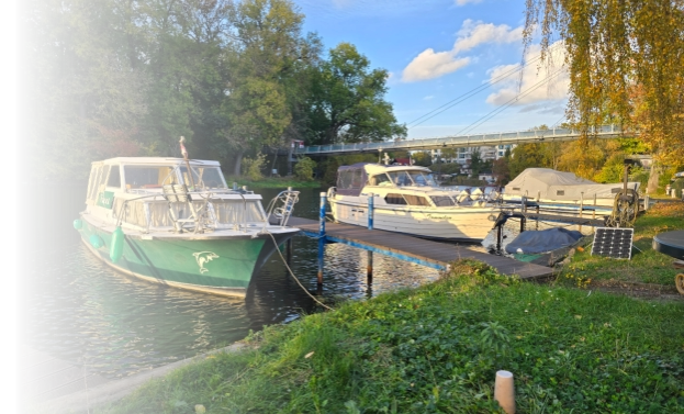 Mehrere Motorboote liegen an den Gastliegeplätzen eines grünen Uferbereichs unterhalb einer Fußgängerbrücke an der Saale.